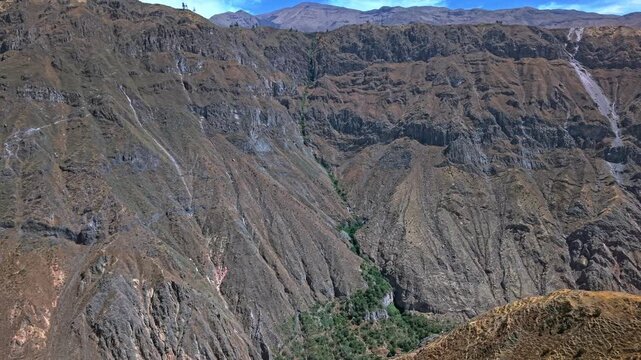 Viewed from opposite canyon wall a thin green lifeline pours into Colca Canyon floor spreading into lush vegetation like water flowing from a tap Golden ridge lines and immense cliffs rise in distance