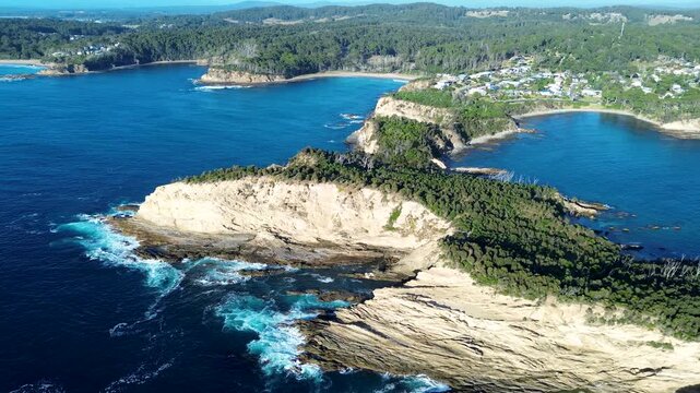 Drone aerial landscape showing ocean waves crashing onto rocky reef and cliff face along Munjip trail at Malua Bay with bushland forest headland coastline South Coast Australia travel tourism nature