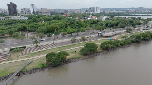 Porto Alegre waterfront boardwalk and Beira Rio avenue traffic captured in aerial lateral parallel flight. Features urban infrastructure under overcast sky. Recorded in 10-bit D-Log 4K video.