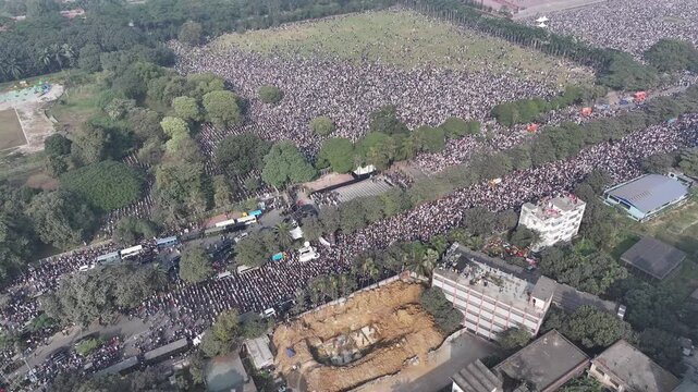 Aerial view of a large crowd gathered on a field near the Jatiya Sangsad Bhaban, creating a mesmerizing contrast against the surrounding greenery, Dhaka, Bangladesh.
