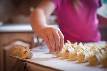 A young person carefully places handmade dumplings on a wooden surface in a cozy kitchen