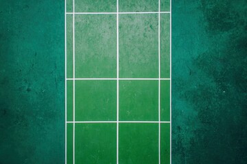 A vibrant overhead view captures the textured green surface of a court, clearly defined by crisp white boundary lines. The geometric patterns and worn details of the playing field suggest dynamic acti