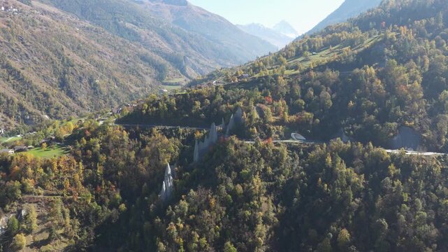 Aerial view of the striking Pyramides d'Euseigne, a geological wonder amidst lush forests and winding roads, showcasing nature's artistry, Heremence, Valais, Switzerland.