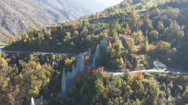 Aerial view of the striking Pyramides d'Euseigne rising amidst the autumn foliage, with a road and tunnel visible, Heremence, Valais, Switzerland.