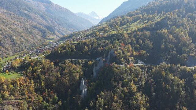 Aerial view of the Pyramides d'Euseigne, with a winding road bisecting the landscape, surrounded by trees in shades of green, Heremence, Valais, Switzerland.