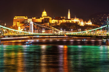 Fototapeta premium Panoramic view of Budapest city and the Danube River at night, Liberty Bridge, tour boats, urban architecture with beautiful illumination, street lights and road traffic