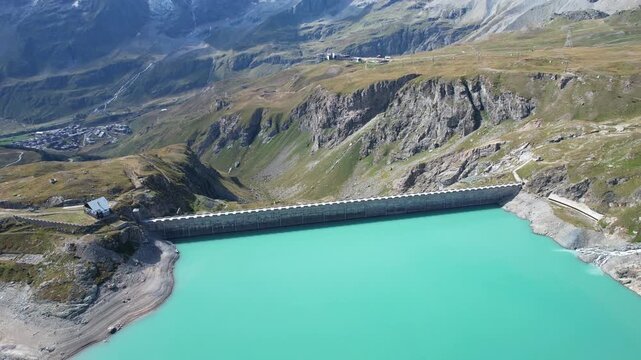 Aerial view of the Diga del Goillet dam holding back a turquoise lake, contrasting with the rugged mountain landscape, Diga del Goillet, Valle d'Aosta, Italy.