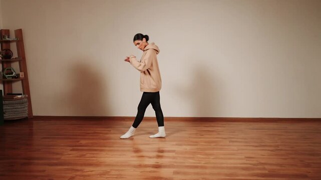 Woman dances in empty dance hall at evening time with simple moves and focused expression