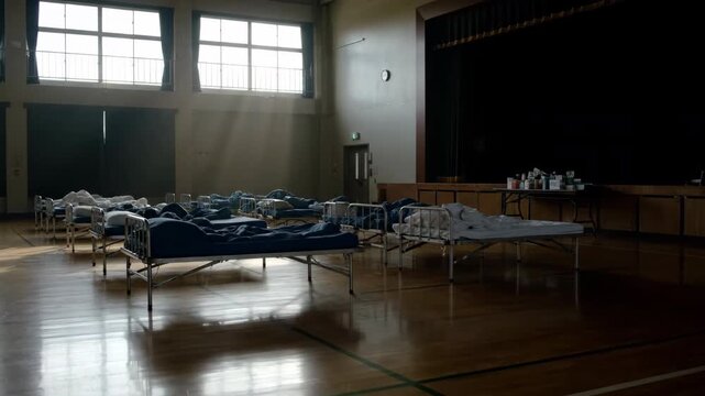 Indoor gymnasium setup as a temporary shelter with rows of cots and supply stations under natural light, ready for emergency aid.