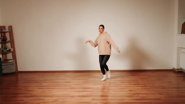 Woman dances alone in a dance hall with wooden floor and simple backdrop