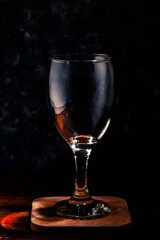 A glass of wine on a wooden coaster against a dark, dramatic background