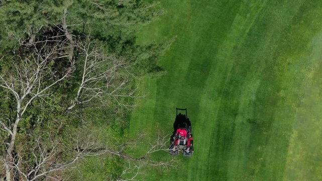 Aerial view of a red lawn mower cutting lines into a vibrant green lawn, creating a geometric pattern of light and dark shades, Boston, Massachusetts, United States.