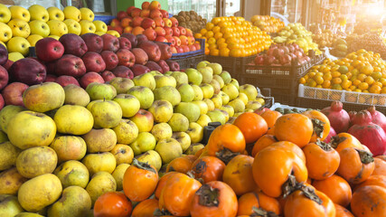 Colorful display of fresh apples citrus and persimmons at local fruit market stall in warm sunlight, seasonal harvest, healthy food concept, abundance of produce, vibrant marketplace atmosphere