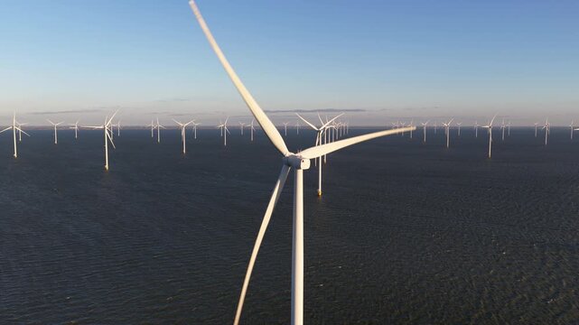 Aerial view of many wind turbines standing tall in the dark ocean water under a clear blue sky, Breezanddijk, Friesland, Netherlands.