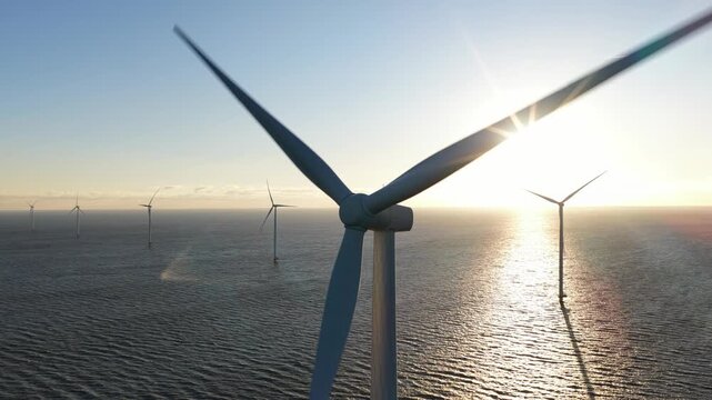 Aerial view of offshore wind turbines standing tall in the shimmering sea as the sun casts a golden glow, Breezanddijk, Friesland, Netherlands.