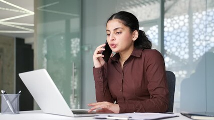 Busy businesswoman multitasking talking on smartphone and working on a laptop while sitting in modern office workplace. Young female employee having business calls, manages tasks, using computer. - Powered by Adobe