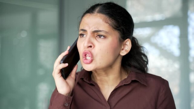 Angry businesswoman arguing talking on mobile phone sitting at workplace in modern office. Frustrated young female manager dealing with stressful business situation or conflict resolution. Close up