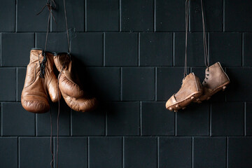 Leather boxing gloves and retro rugby boots hang on a black wall in a gym