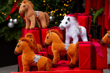 Plush brown and white horses in a red cart with boxes of gifts against a background of pine needles decorated with silver balls and garlands