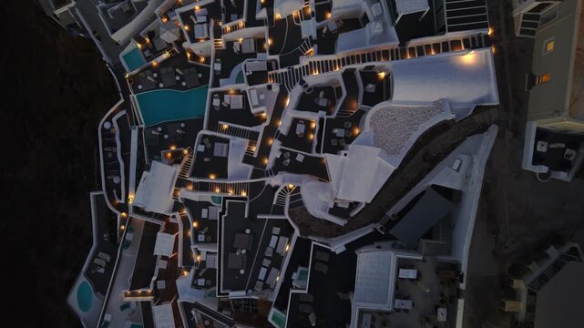 Aerial view of the white washed buildings and illuminated pathways in Imerovigli, creating a captivating contrast against the dark landscape, Imerovigli, Thira, Greece.