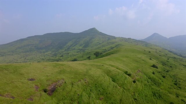 Aerial dolly in over rolling green hills and distant peaks in Sanjay Gandhi National Park, India
