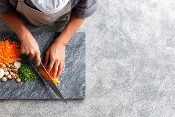 Chef hands chopping fresh carrots, preparing healthy vegetables on dark stone cutting board