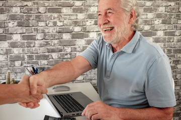 Mature businessman working at his desk while shaking hands with a client who is finalizing a contract. Office concept, close-up, business, transactions.