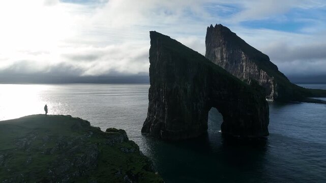 Aerial view of the dramatic Drangarnir sea stack with its arch, contrasting against the dark ocean and cloudy sky, Faroe Islands.