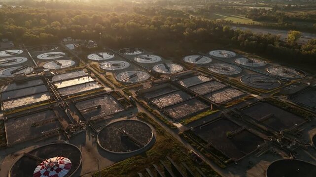 Aerial view of the wastewater treatment plant's circular and rectangular tanks, reflecting the sky, surrounded by trees, Turin, Piemonte, Italy.