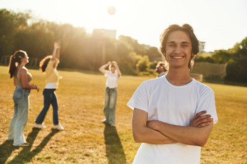 Guy is standing in front of other people. Young friends are having fun on the field