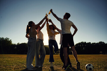 Against sunlight. Dark photo of people cheering, celebrating, holding beer bottles