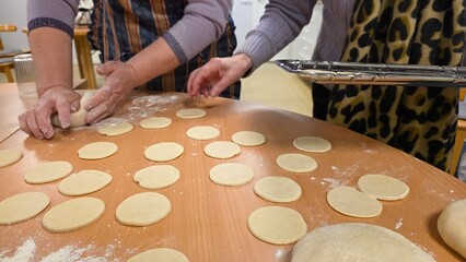 Making dough circles in a kitchen with two people preparing food on a table covered in flour in a casual setting