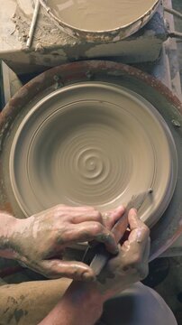 A craftsperson shapes clay on a pottery wheel, their hands skillfully guiding the emerging form. The spinning wheel and wet clay create a dynamic scene, highlighting the artistry.
