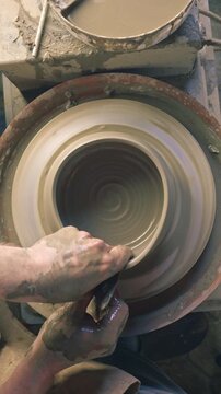 A medium close-up of a craftsperson's hands shaping clay on a pottery wheel, creating a smooth, symmetrical form. The workshop setting, with tools and clay, emphasizes the art of pottery.