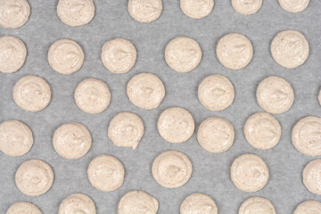 A high angle shot of several rows of unbaked beige french macaroon batter portions piped onto white parchment paper on a baking sheet