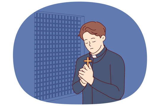 Padre prays and holds christian cross in hands, standing in confession room, asking god to atone for sins of temple visitors. Catholic priest observes ritual of confession and reads prayer