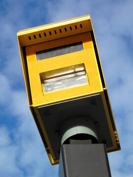 A fixed yellow road speed camera on a roadside pole for traffic law enforcement speeding, monitoring vehicle speeds to ensure road safety and compliance in the UK, stock photo image