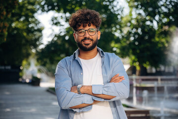 Arms crossed, standing. Handsome man is outdoors in the city