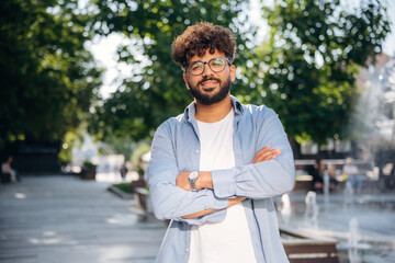 Looking at the camera, standing. Handsome man is outdoors in the city