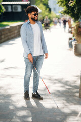 Under beautiful sunlight, walking. Blind man with white cane and sunglasses is in the city