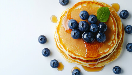 Delicious pancakes piled high with fresh berries and syrup, viewed from above on a white surface