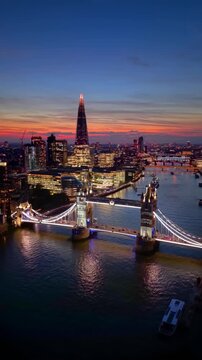 Aerial view of the illuminated Tower Bridge, River Thames and City skyscrapers in London, England, during dusk twilight