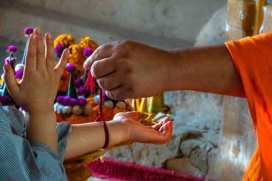 Senior monk attaching a red buddhist bracelet string during a ceremony in Wat Chomphet, on top of a hill across the Mekong River from Luang Prabang, Laos