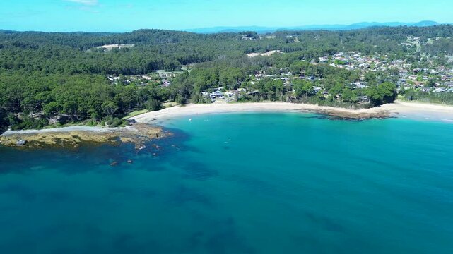 Drone aerial landscape showing Wimbie Beach coastline including rocky ocean reef and bushland trees with town neighbourhood suburbs of Surf Beach in Batemans Bay Australia travel tourism holidays