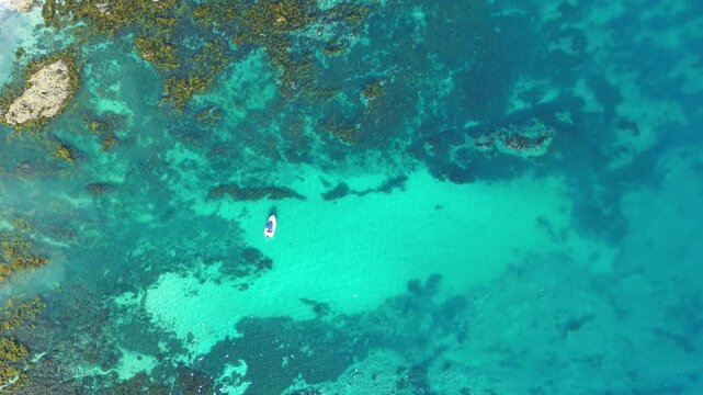 Drone aerial landscape of boat driving along water surface in the middle of an ocean bay cove with seaweed covered rocks and clear reef sandbar in Batemans Bay NSW Australia travel marine tourism