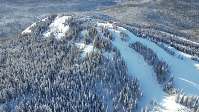 A very wide, aerial shot captures a vast, snow-covered mountain landscape and ski resort, including slopes and a dense winter forest, likely near Mount Sima, Yukon