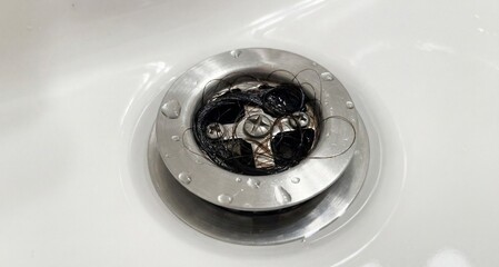 Clogged hair in bathtub drain with water and metal strainer  