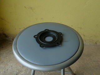 Black rubber gasket with holes placed on a metal stool seat indoors.