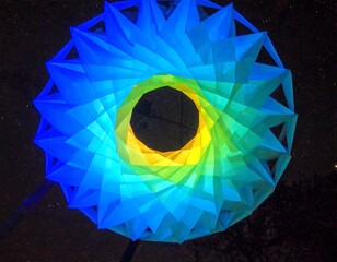 Aerial view of a colorful, geometric, star-shaped structure lit from within, against a dark sky