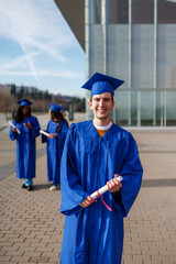 Happy student in graduation gown holding diploma with friends in front of a modern building